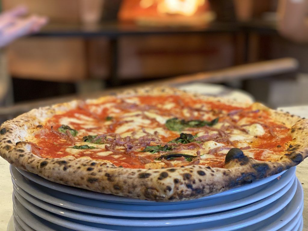 Pizza su una pila di piatti bianchi davanti a un forno a legna.