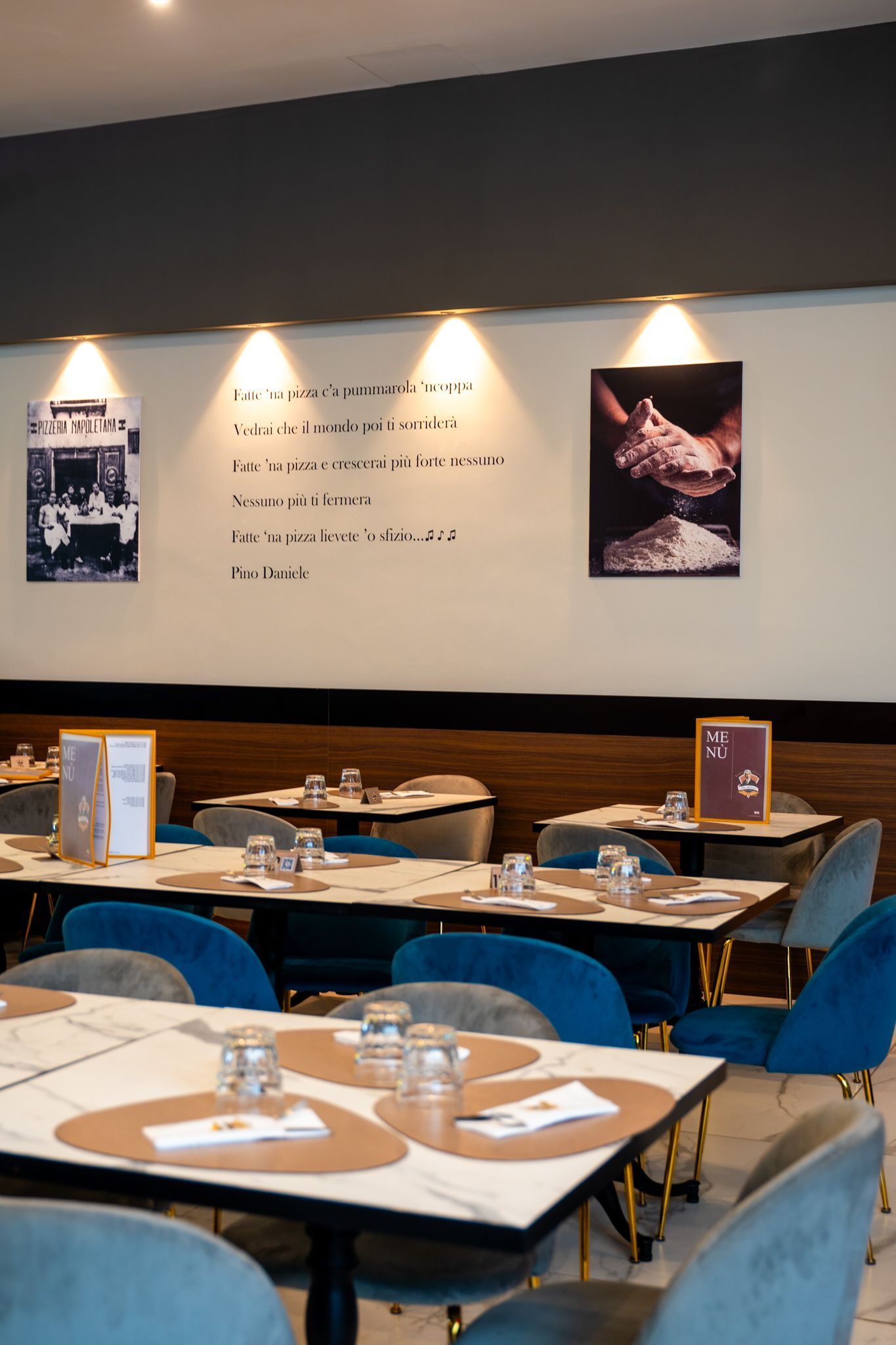 Interno del ristorante con tavoli, sedie in velluto blu, opere d'arte e illuminazione dall'alto.