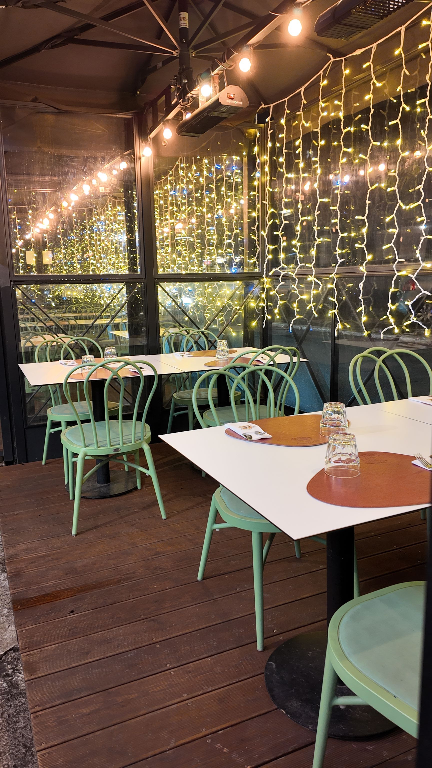 Posti a sedere all'aperto del ristorante con sedie e tavoli verdi, decorati con luci a stringa.