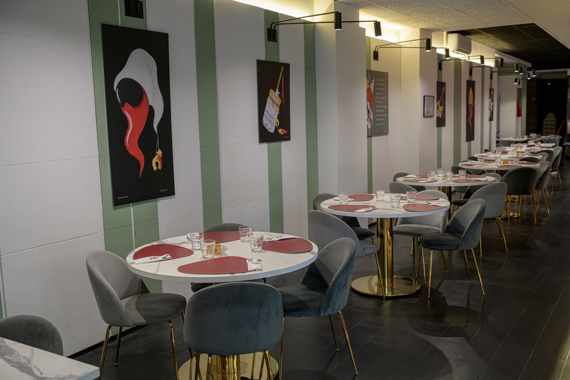 Sala da pranzo del ristorante con tavoli rotondi, sedie e opere d'arte sulle pareti a strisce.