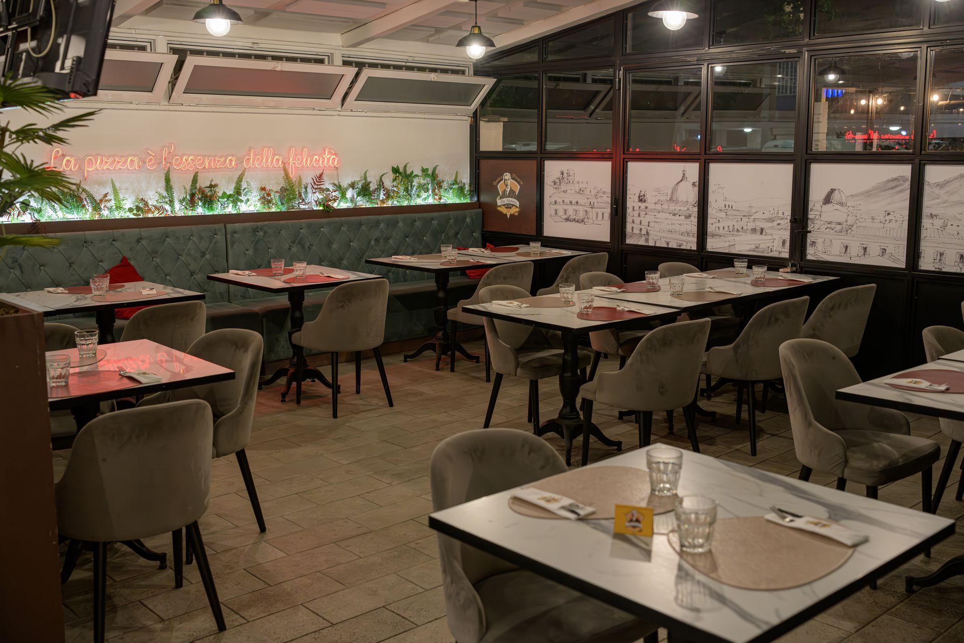 Interno di un ristorante con tavoli apparecchiati per cenare, luci soffuse e piante decorative.