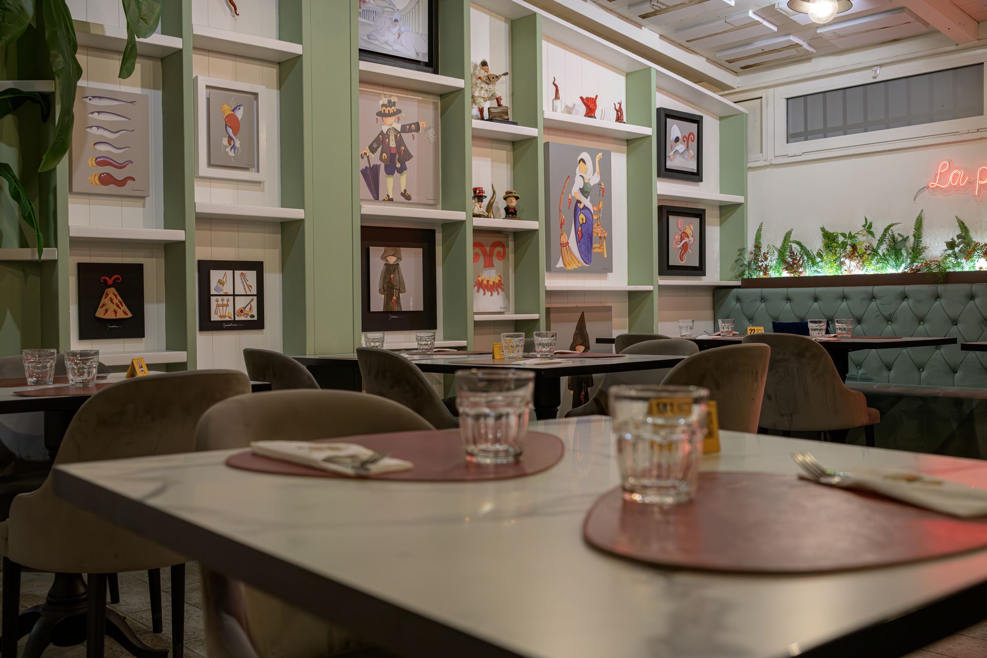 Interno del ristorante con tavoli apparecchiati, opere d'arte alle pareti e dettagli verdi.