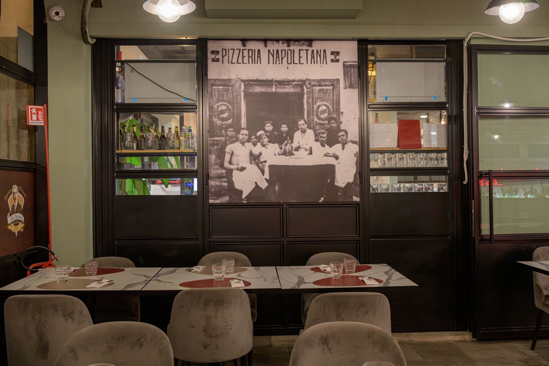 Zona pranzo con tavoli apparecchiati per gli ospiti, incorniciati da una foto d'epoca e da infissi in metallo scuro.