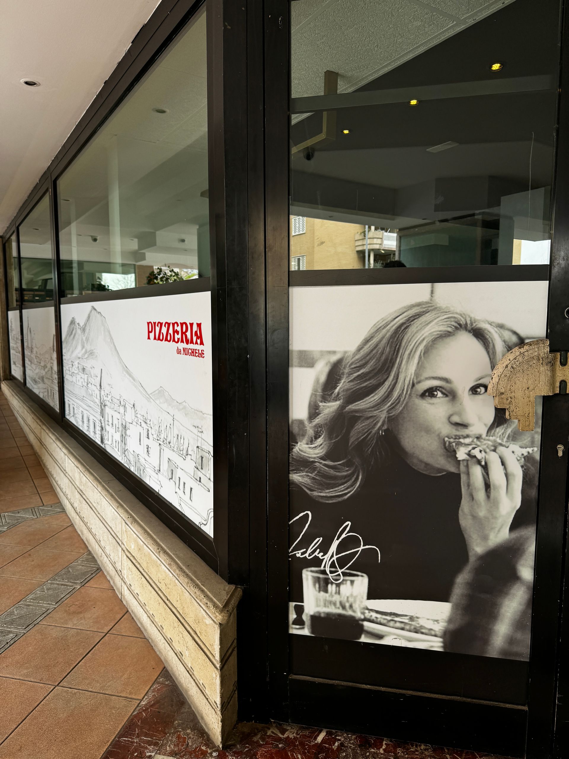 Vetrina di un ristorante con una donna che mangia una pizza e disegni architettonici.