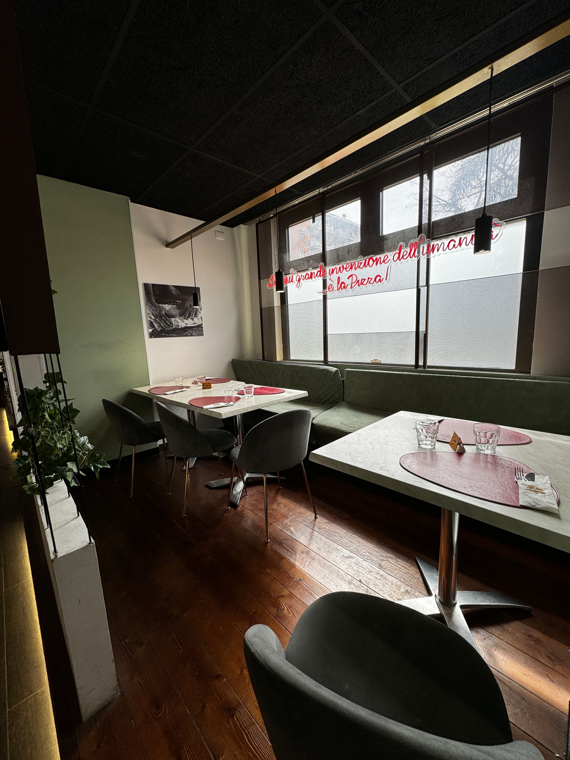 Interno di un ristorante con tavoli, sedie e posti a sedere vicino alla finestra. Pavimenti in legno scuro, pareti verdi e bianche.