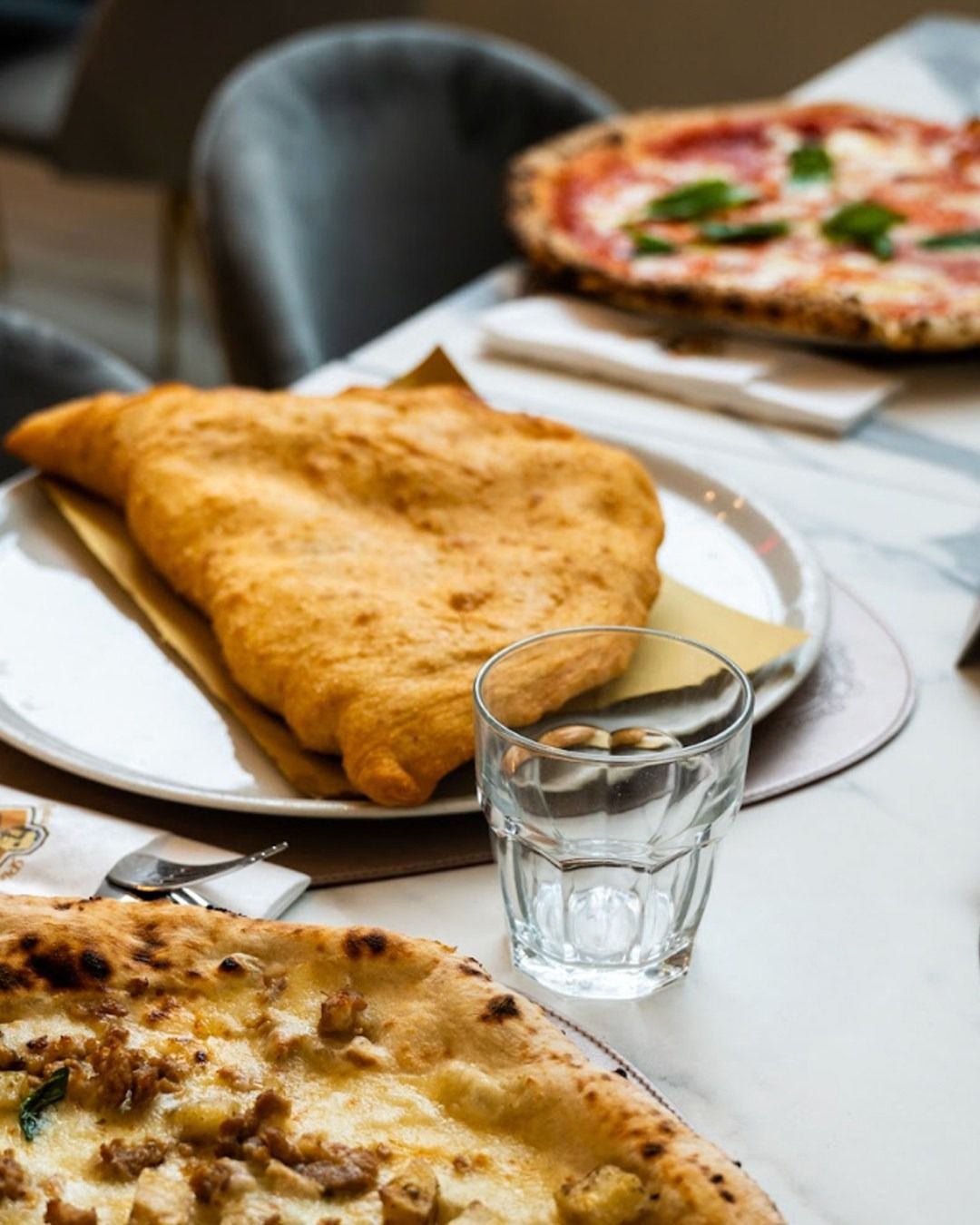 Primo piano di pizza fritta, pizza e un bicchiere d'acqua su un tavolo di marmo bianco.