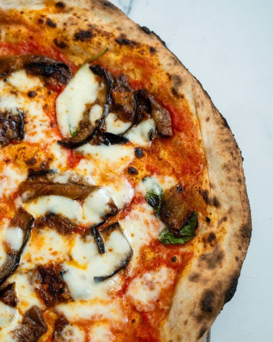 Pizza con mozzarella, melanzane e salsa di pomodoro; la crosta è bruciacchiata.
