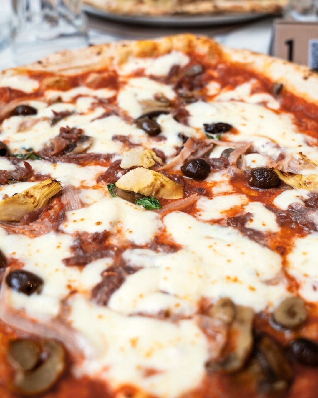 Primo piano di una pizza con formaggio, olive, funghi, cuori di carciofo e carne.