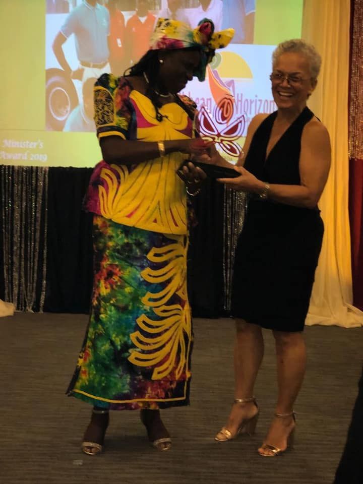 A woman in a colorful dress is receiving an award from another woman