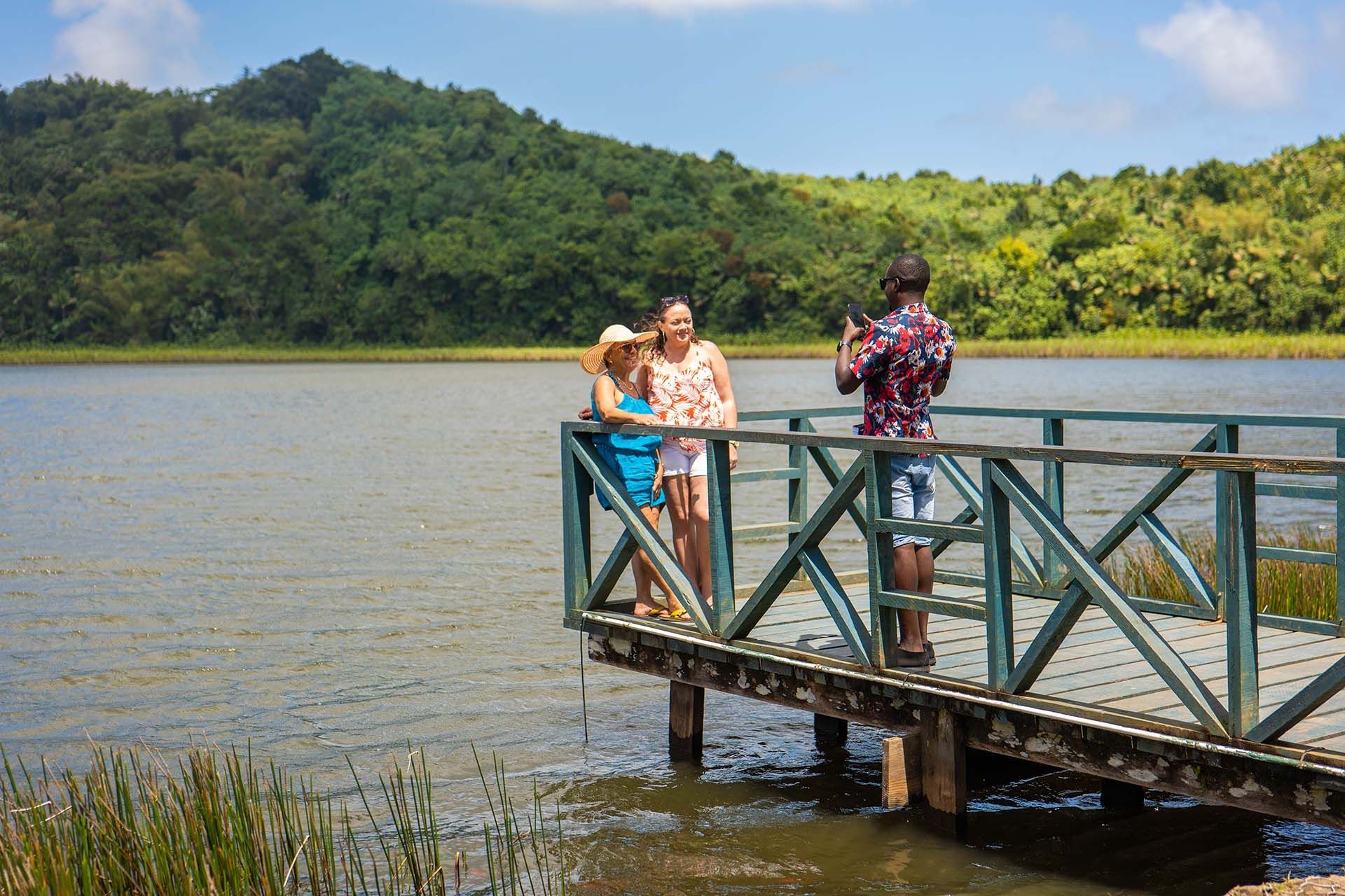 A man is taking a picture of two women standing on a dock overlooking a lake.