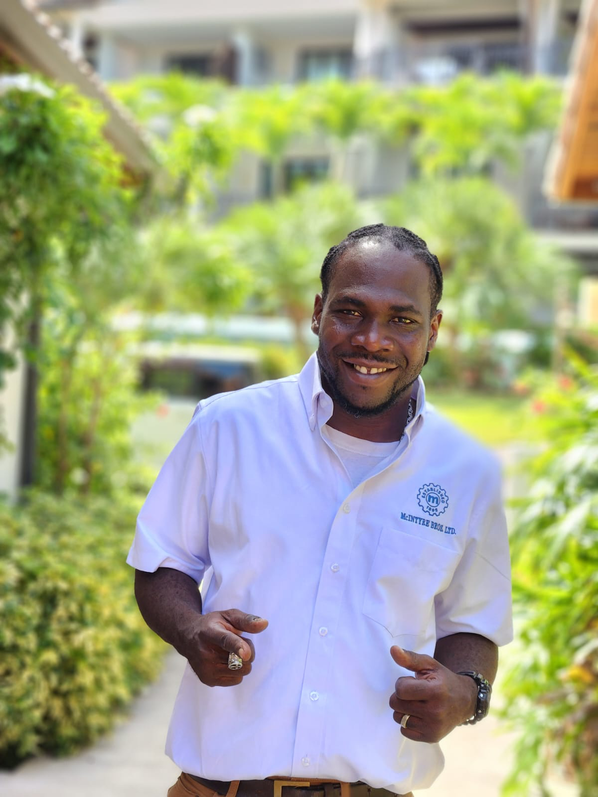 A man in a white shirt is smiling and pointing at the camera.