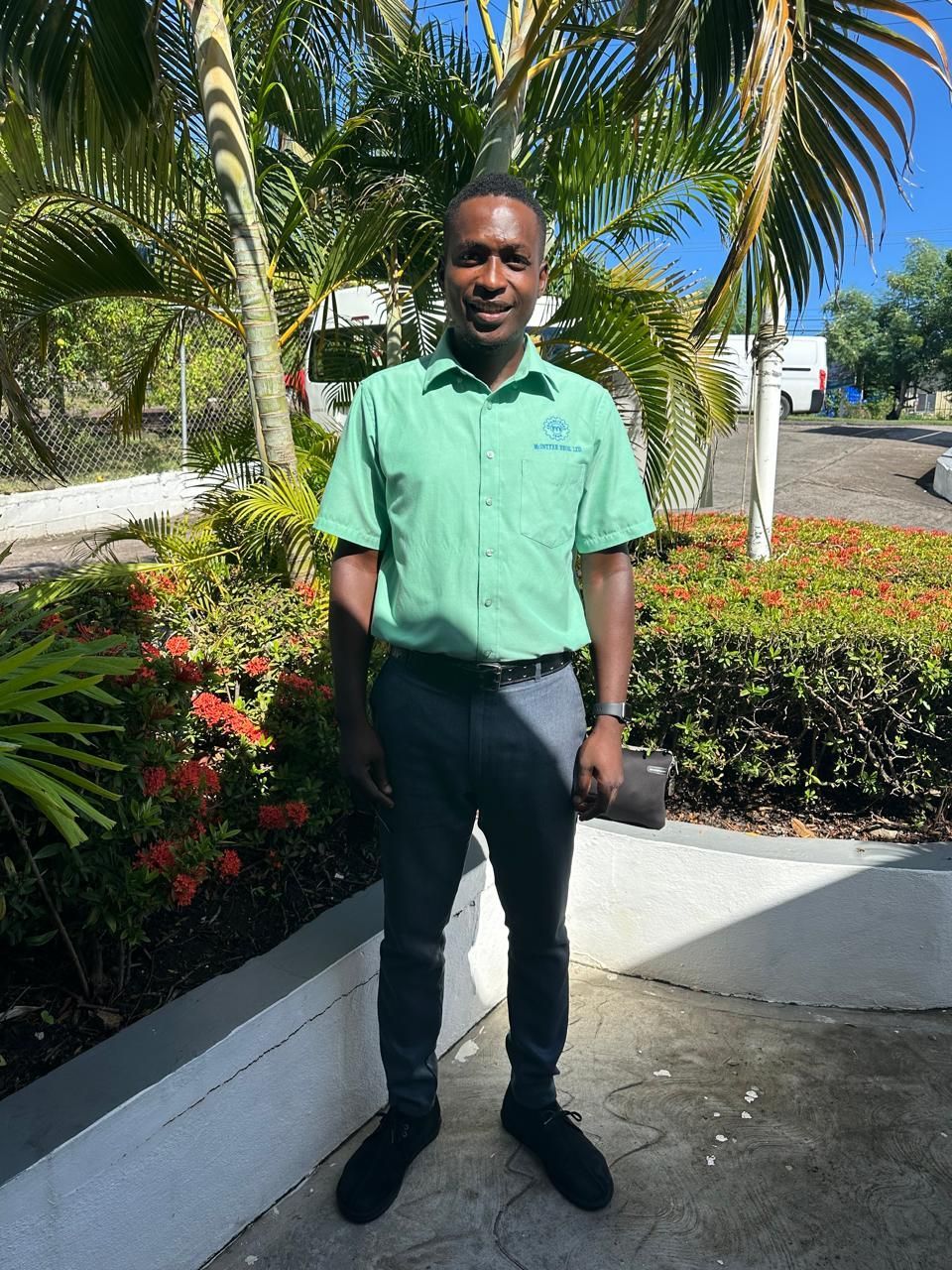 A man in a green shirt is standing in front of a bush with flowers.