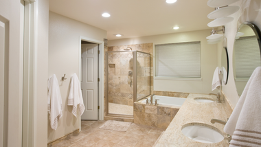 Bathroom with a double sink vanity, shower, tub, and white towels; cream-colored walls.
