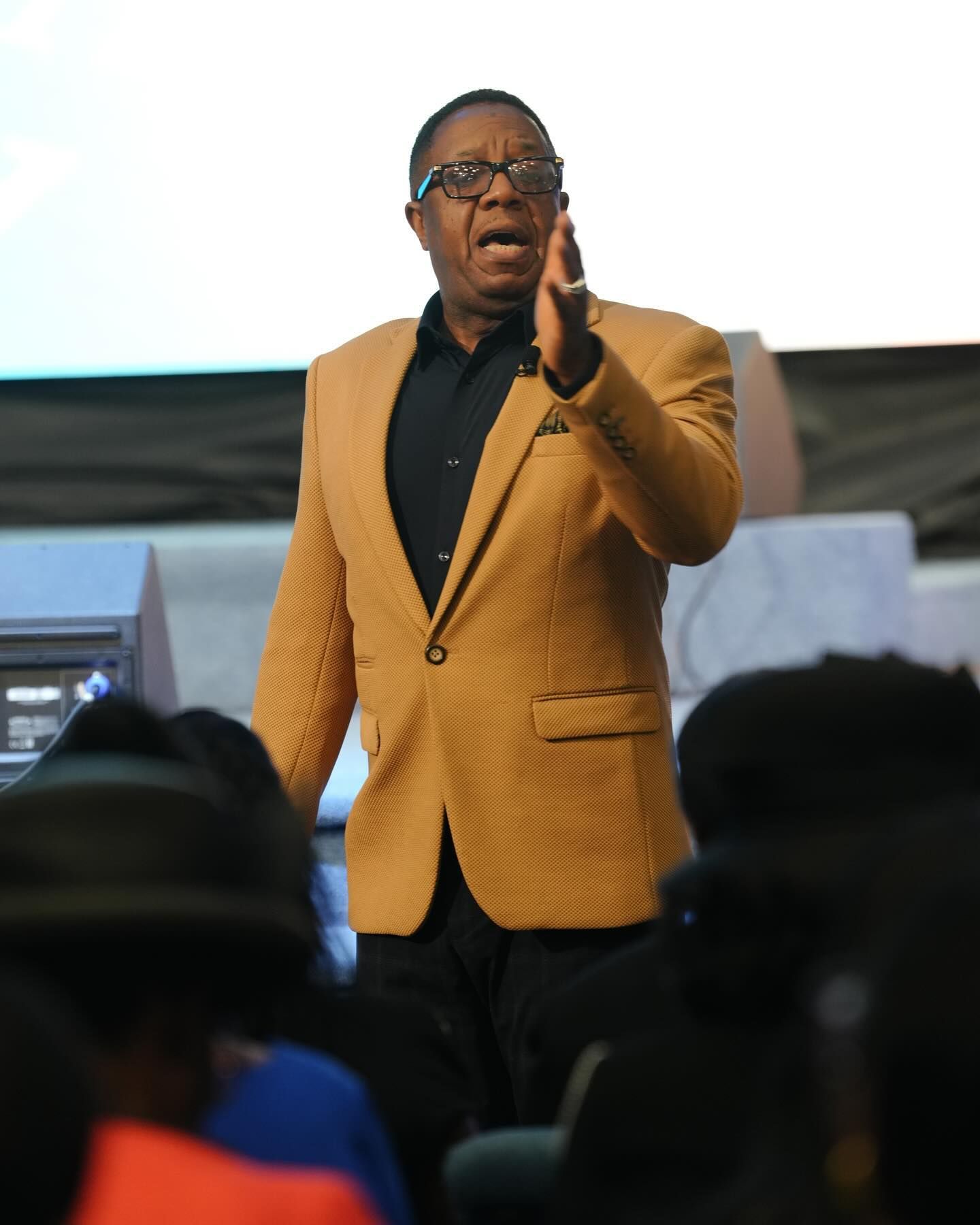 A man in a yellow jacket is giving a presentation to a group of people