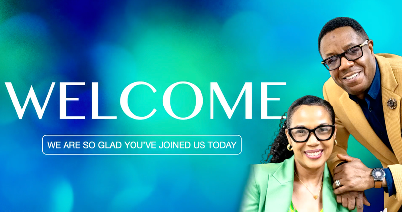 A man and a woman are standing next to each other in front of a welcome sign.
