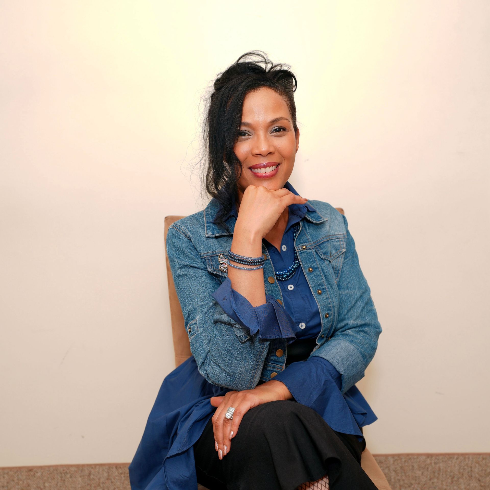 A woman wearing glasses and a green jacket is sitting on a stone wall.