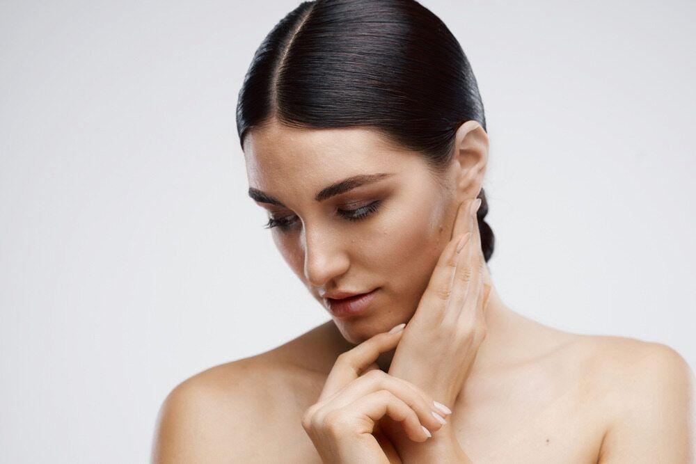 Woman With Dark Hair, Looking Down, Touching Her Neck. Light Skin, Neutral Background — Eternal Radiance in Strathmore, VIC