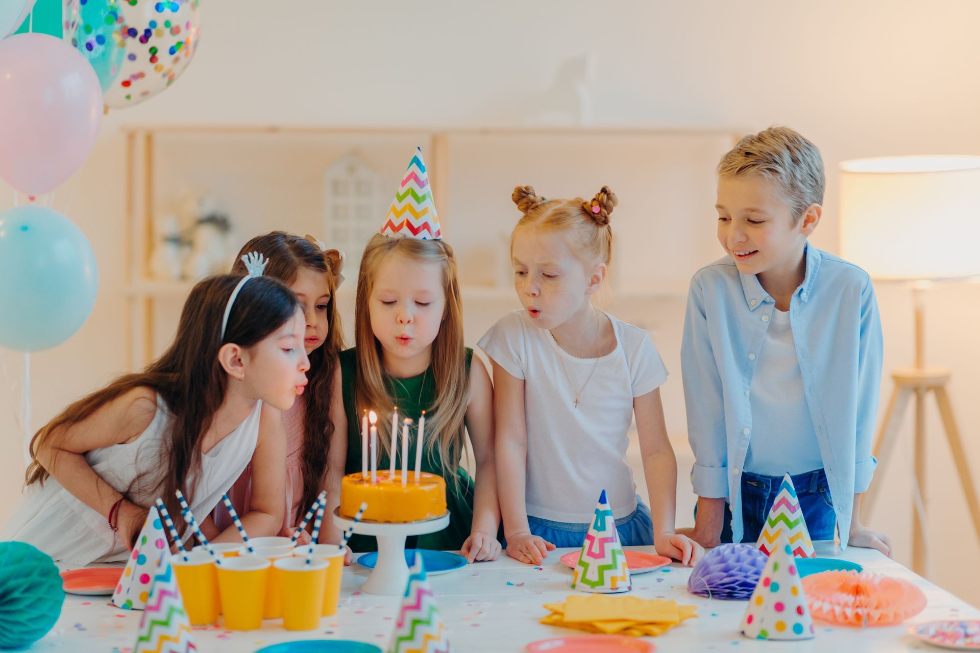a group of children are blowing out candles on a birthday cake .