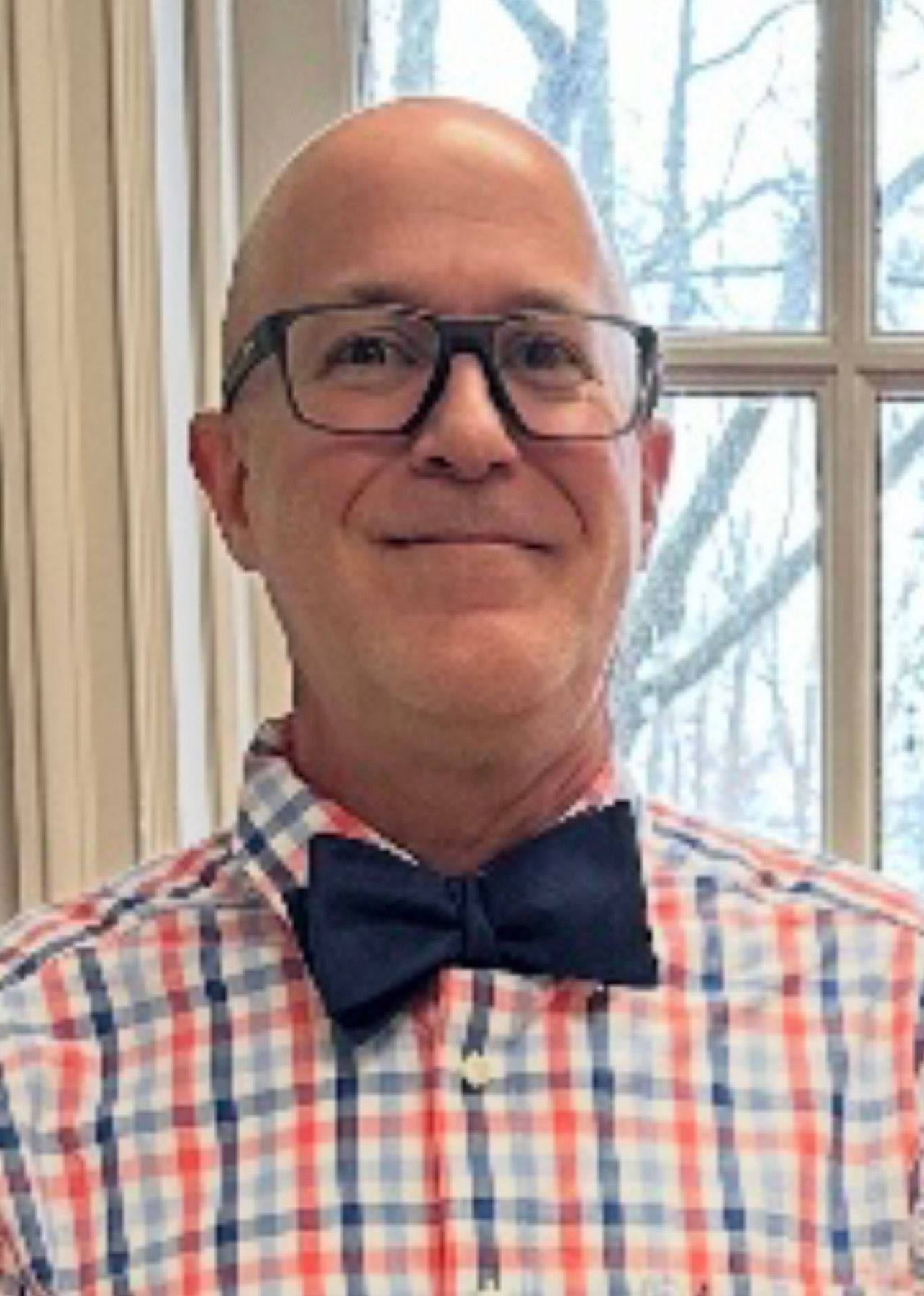 Man in black suit, striped tie, hands in pockets, looking to the side, outdoor setting.