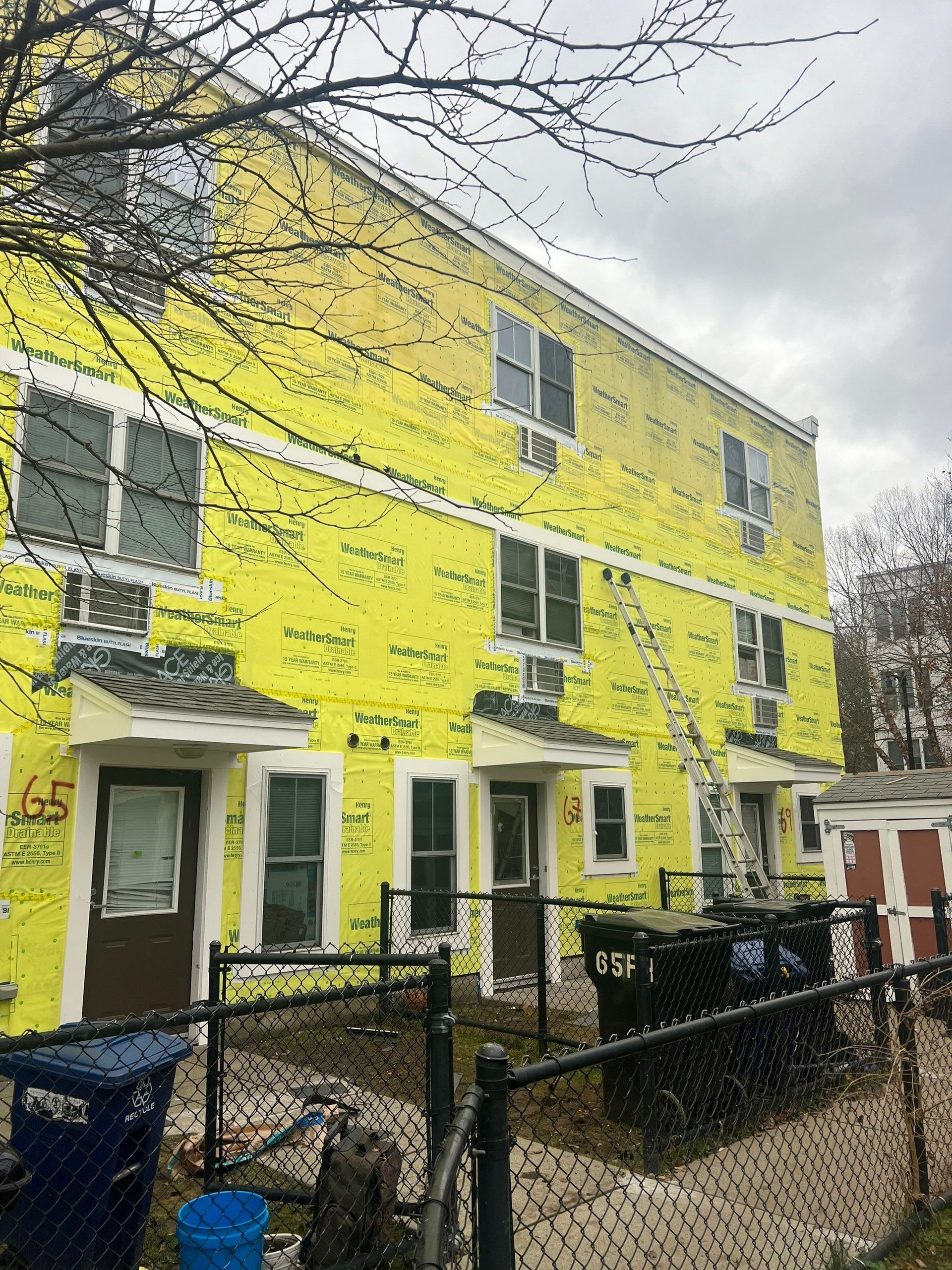Building exterior covered in bright yellow insulation, ladder against the wall, cloudy sky.