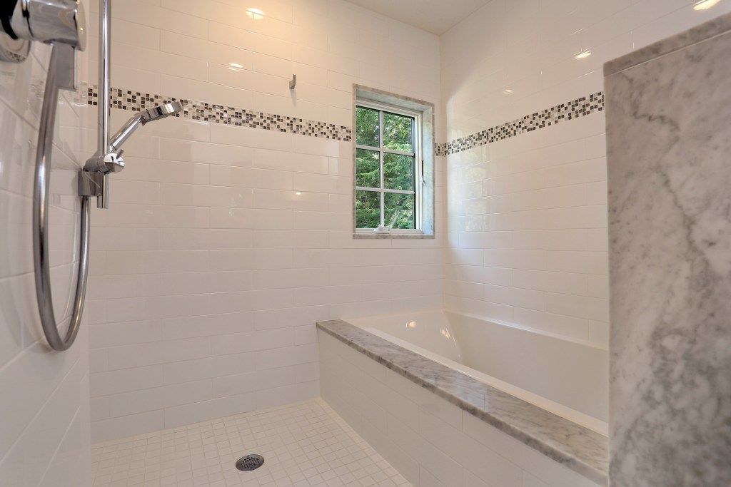 White tiled bathroom with showerhead, small window, and built-in bench. Decorative black and white tile border.