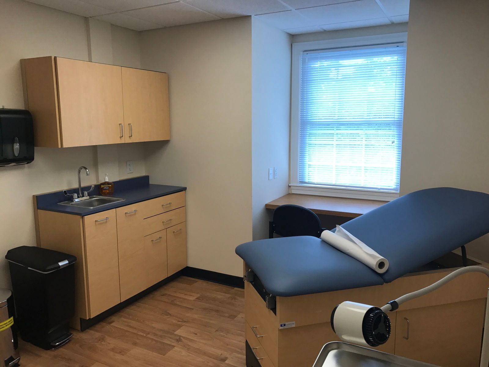 Examination room with cabinet, sink, medical table, and window.