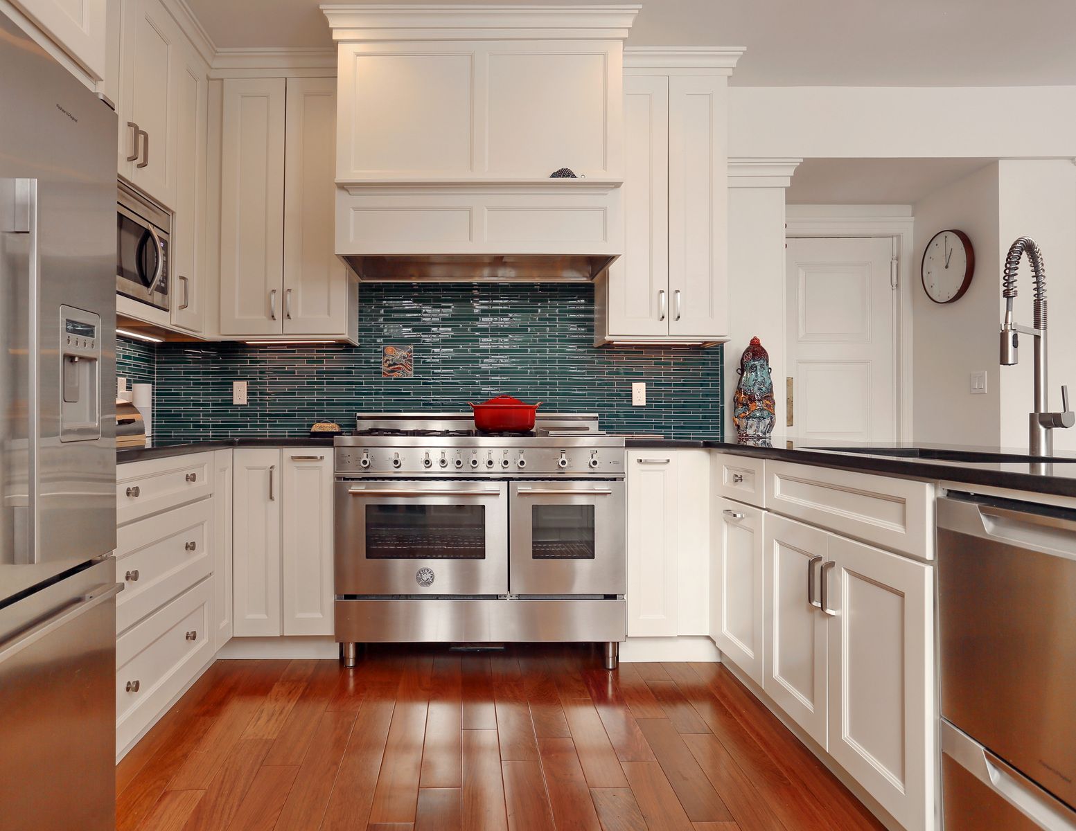White kitchen with stainless steel appliances, blue tiled backsplash, and wooden floors.