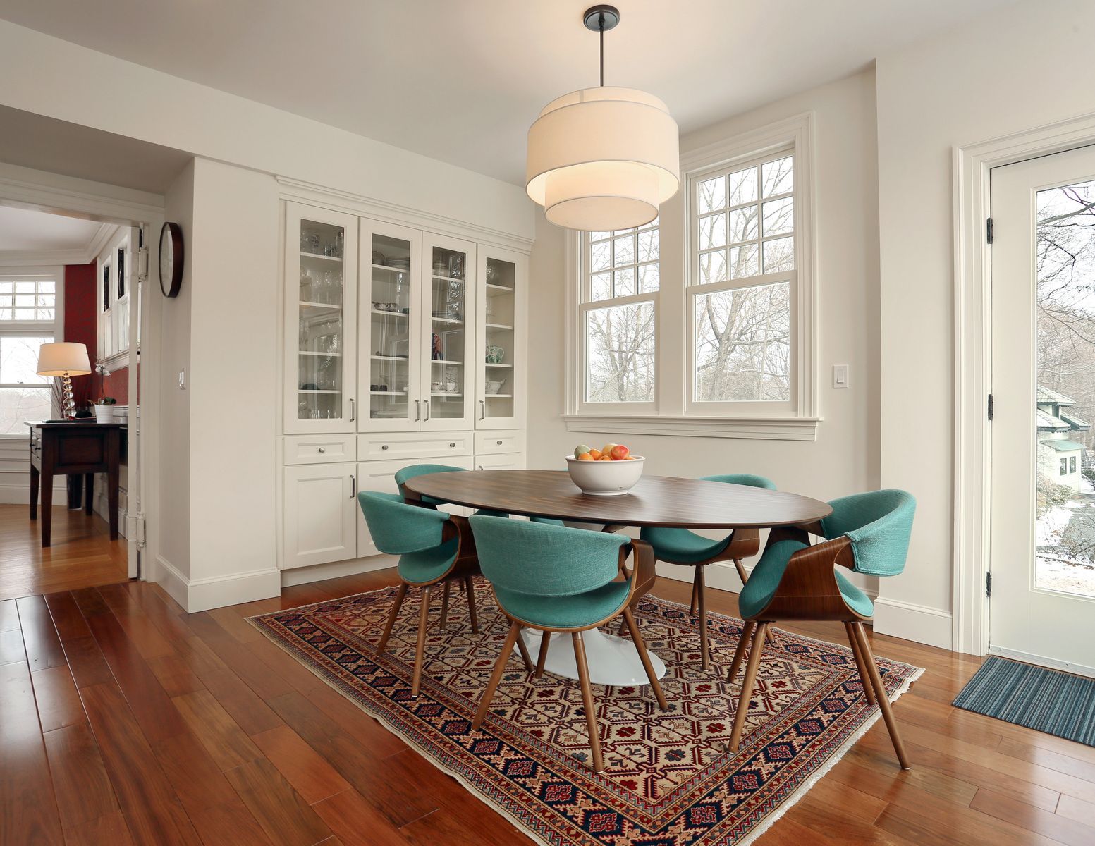 Dining room with oval table, teal chairs, rug, built-in cabinets, pendant light, and a door.