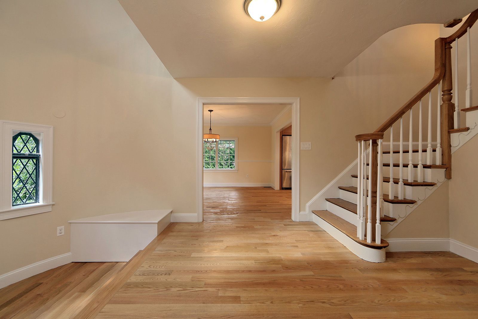 Entryway with wooden staircase, wood floors, arched window, and doorway to another room.