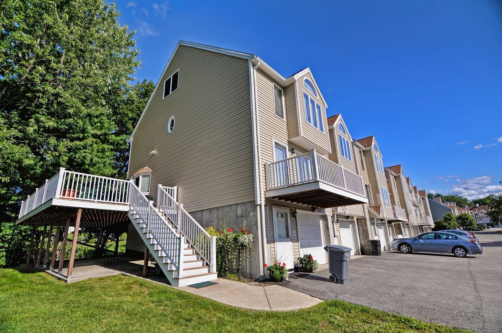 Multi-story townhouses with decks, stairs, and a driveway on a sunny day.