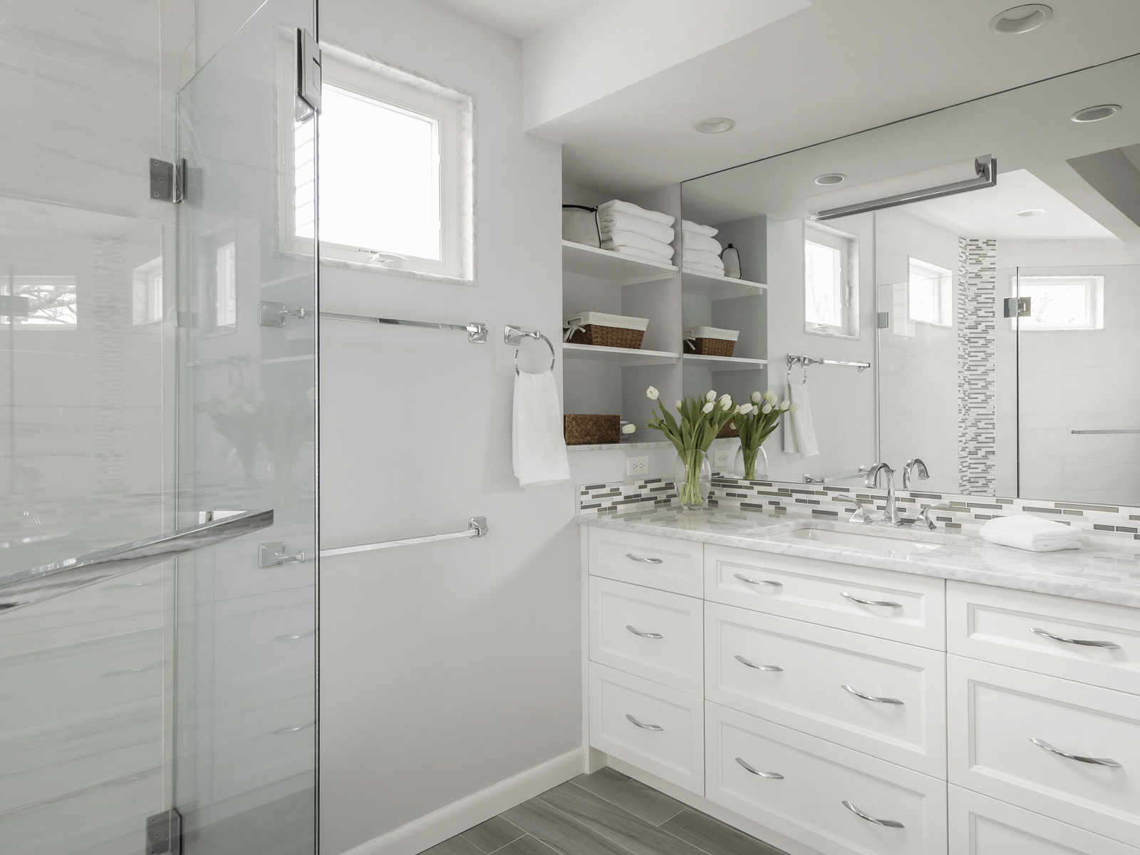 Modern white bathroom with shower, vanity, and open shelving filled with towels and décor.