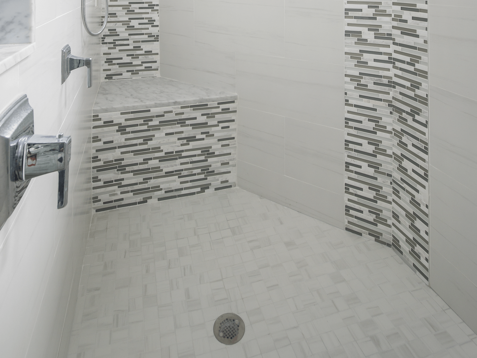 Shower stall with gray and white tile, built-in bench, and chrome fixtures.