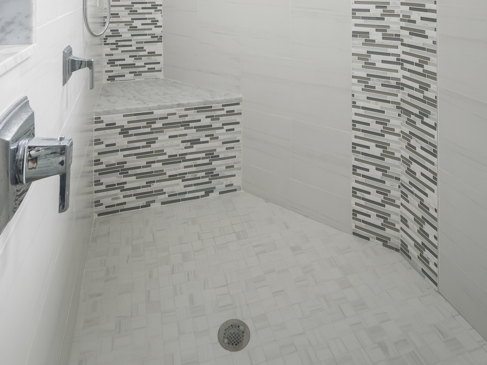 Shower stall with gray and white tile, built-in bench, and chrome fixtures.