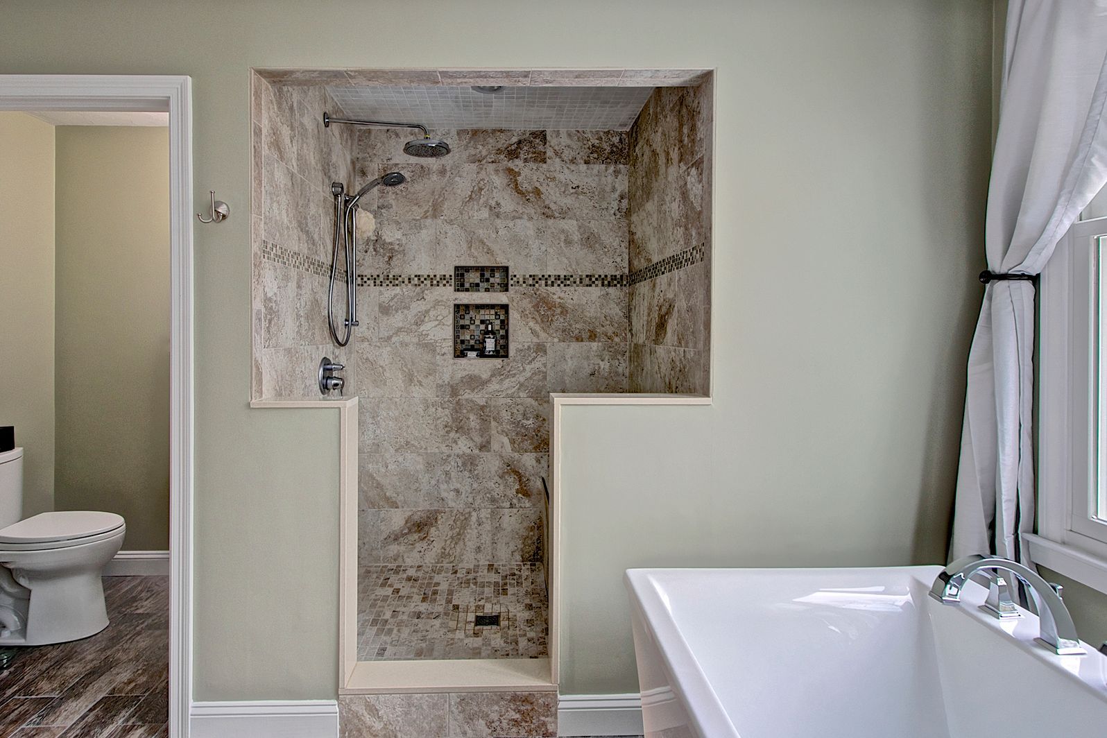Bathroom with recessed shower and soaking tub, soft green walls, and marble tile.