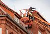 Worker on lift repairing roof of a brick building with orange tile roof.