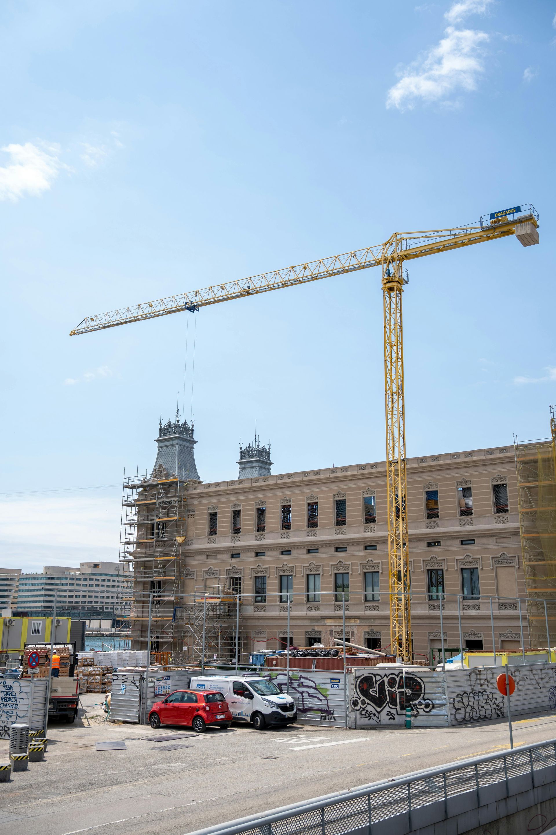 Construction site with a tall yellow crane next to a light-colored building under renovation on a sunny day.