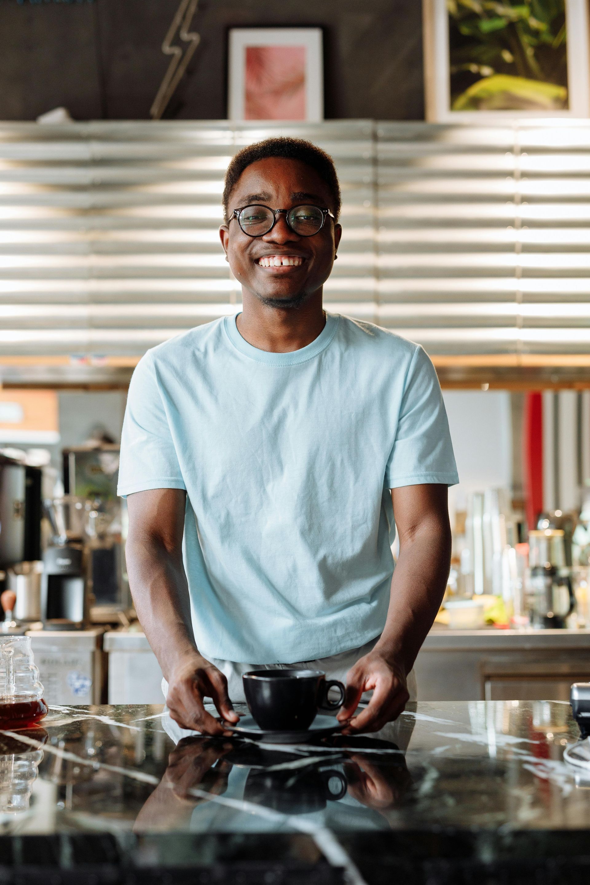 Man holding a black coffee cup, smiling at the camera, inside a cafe.