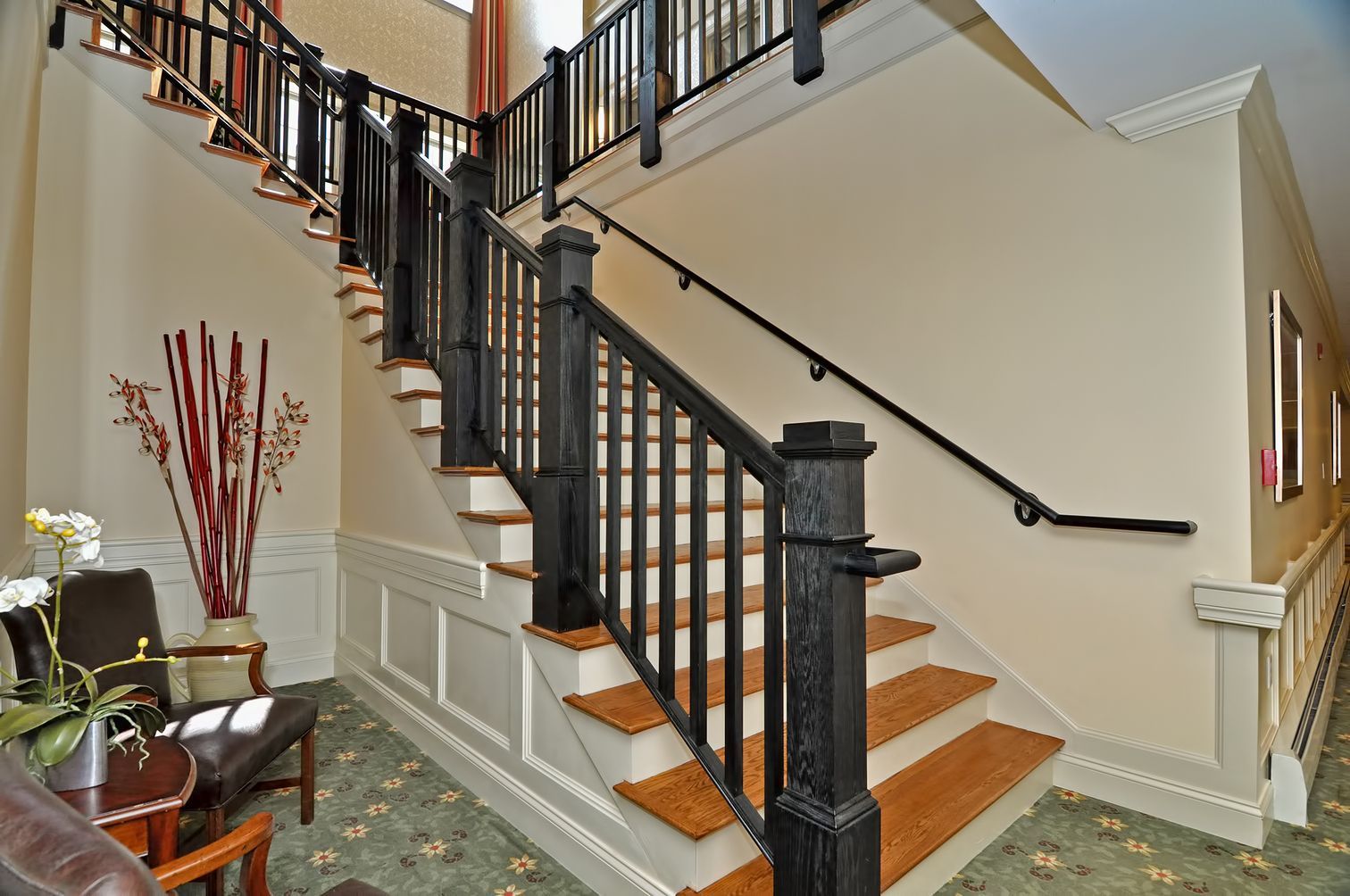 Staircase with black banister, light wood steps, and off-white walls in a building hallway.