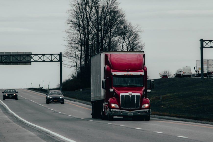 A red semi truck is driving down a highway next to other cars.