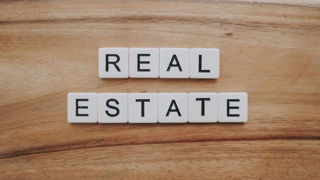 The word real estate is written in scrabble tiles on a wooden table.