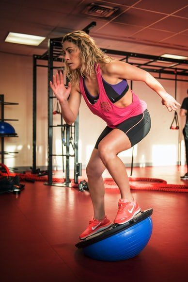 A woman is jumping on a blue balance ball in a gym.
