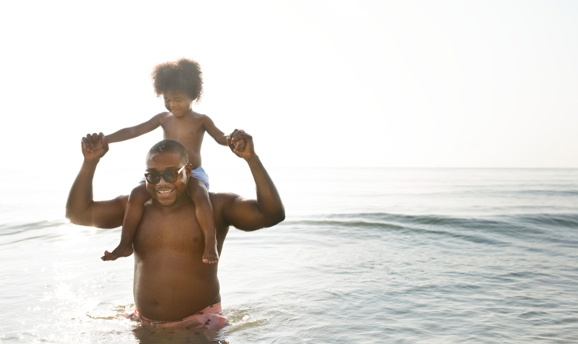 A man is carrying a child on his shoulders in the ocean.