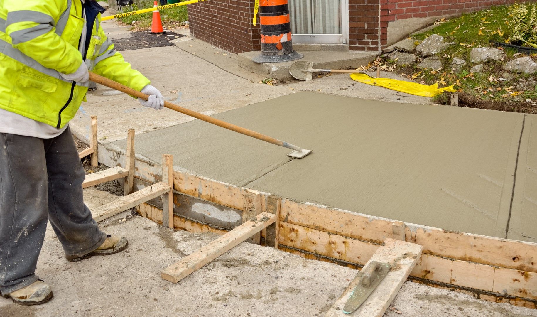 A man is using a rake to spread concrete on a sidewalk.