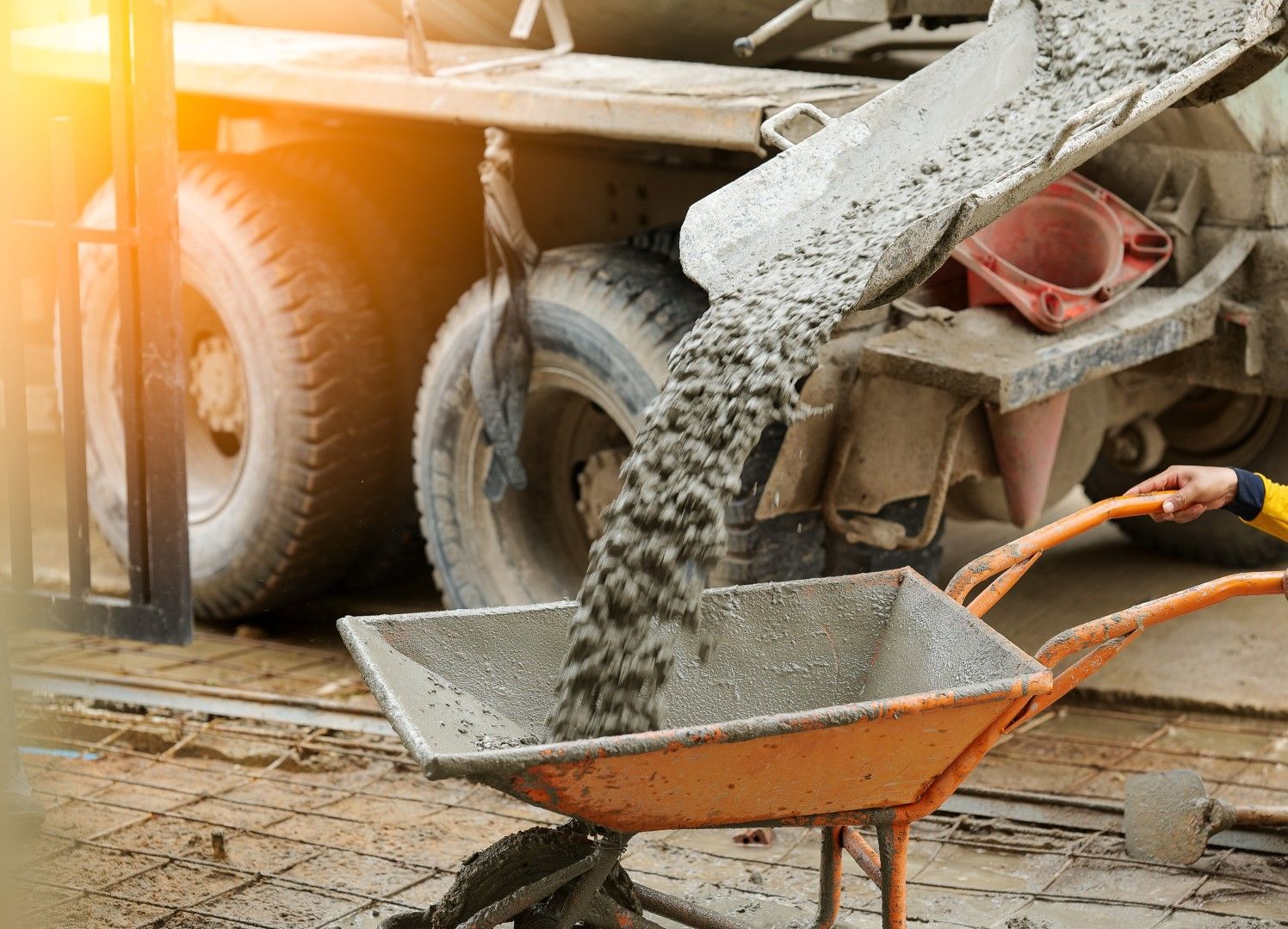 A concrete truck is pouring concrete into a wheelbarrow.