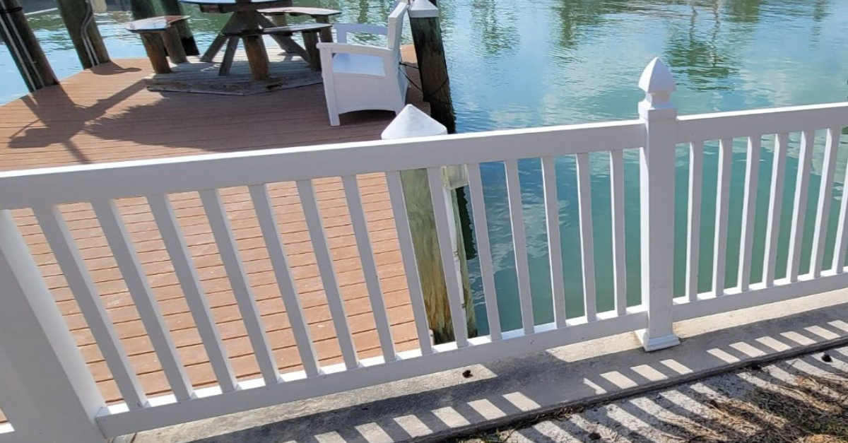 White picket fence along a waterfront dock. Aqua water and wooden structure in the background.