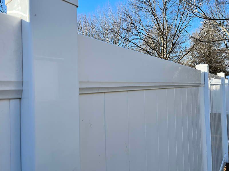 A close up of a white vinyl fence with trees in the background.