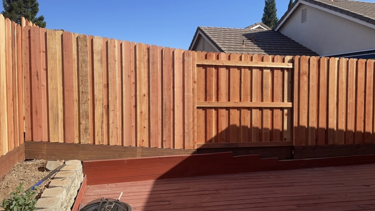 Wooden fence with gate in backyard. Red-brown bricks, brown fence, clear sky.