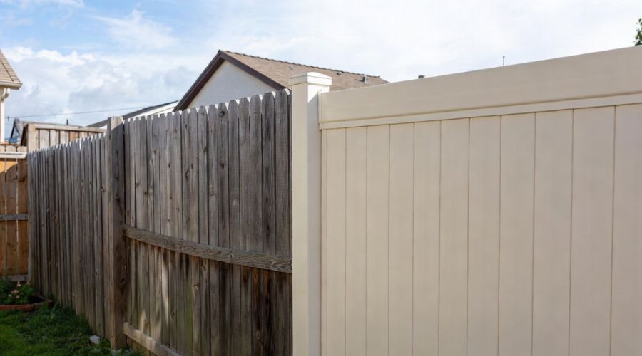 A weathered wooden fence section sits next to a clean, light-colored vinyl privacy fence in a residential backyard.