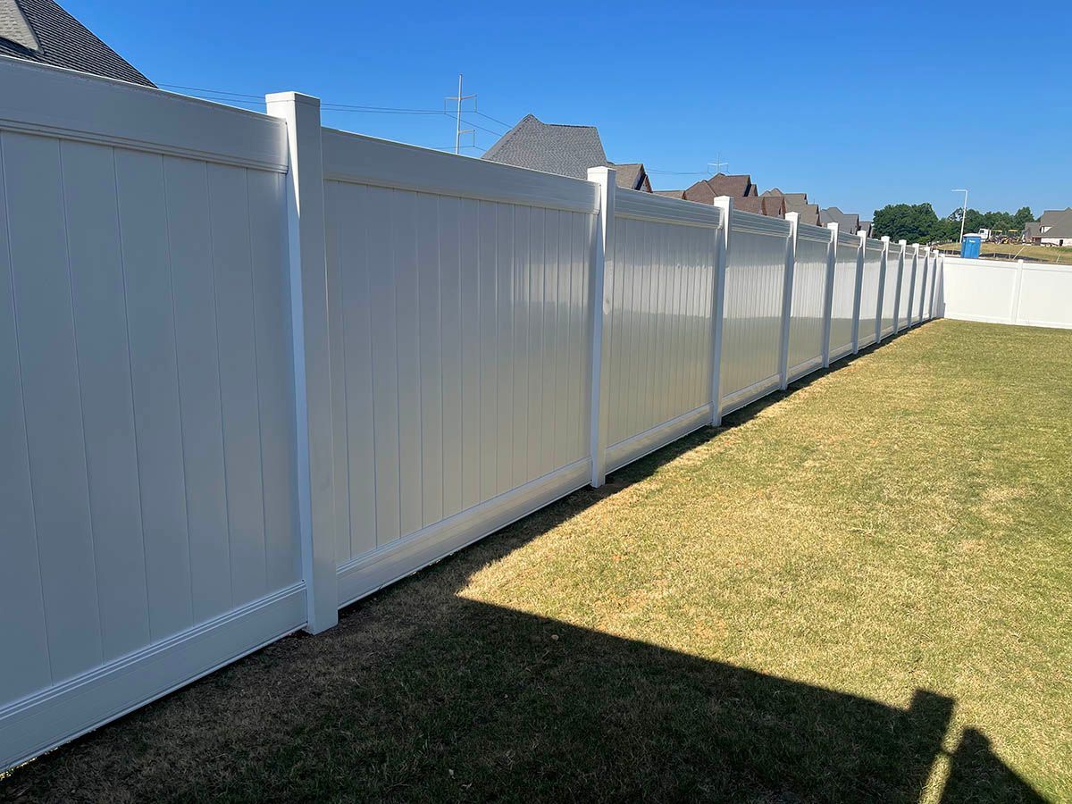 White vinyl fence along a grassy yard under a clear blue sky.