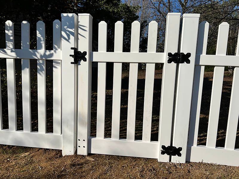 A white picket fence with black hinges is sitting in the dirt.